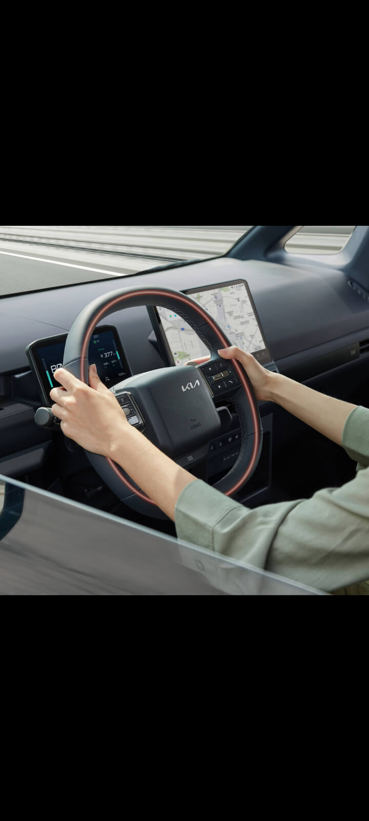 Nahaufnahme des Lenkrads im Kia PV5 Passenger mit den Händen des Fahrers.